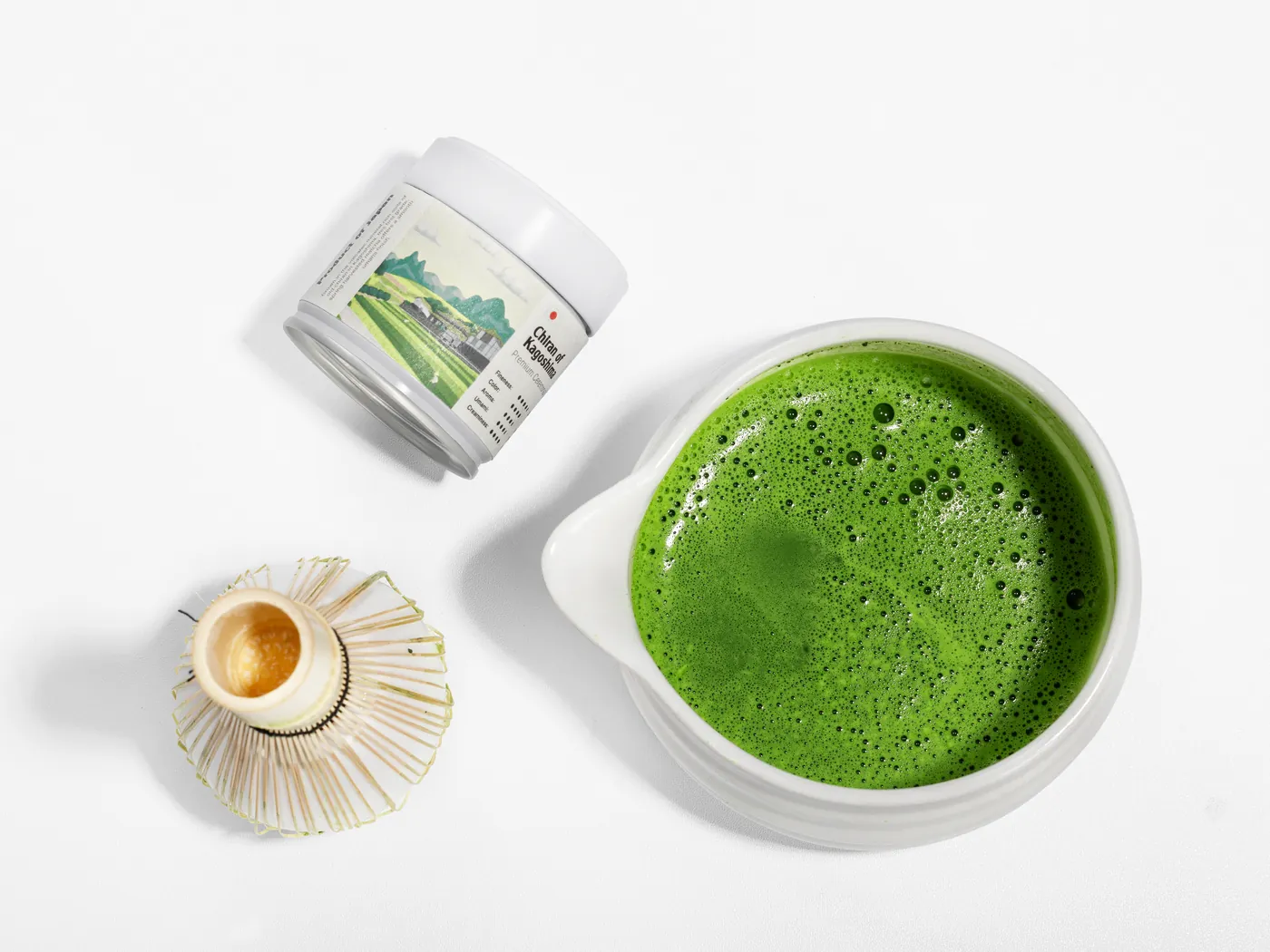 A bowl of freshly whisked matcha next to a bamboo whisk and an M'atelier tin