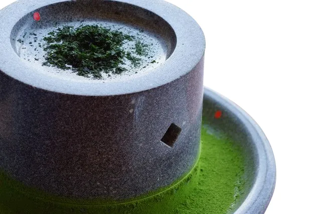 A granite stone mill with tea leaf on top and green powder below